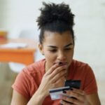 スマートフォンとクレジットカードを手に買い物を迷う人