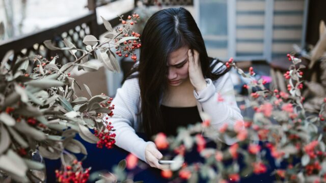 スマートフォンを見て不安そうに頭を抱える人